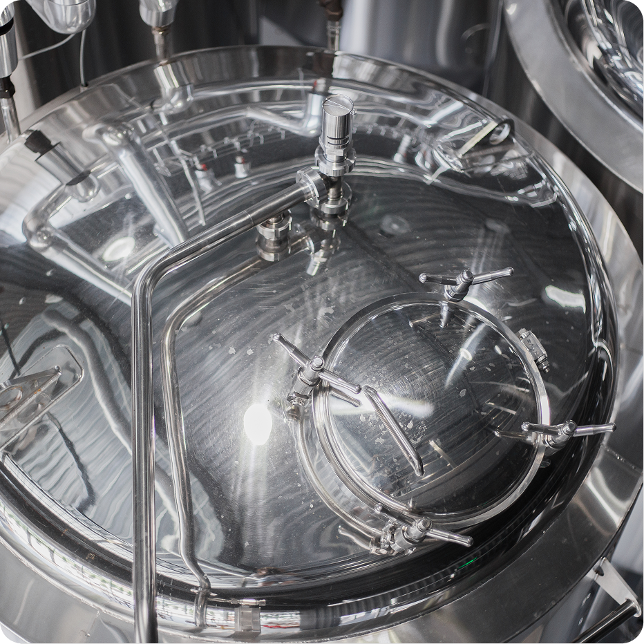 Mann mit Klemmbrett und Stift steht in einer Brauerei neben großen Metalltanks und macht Notizen.