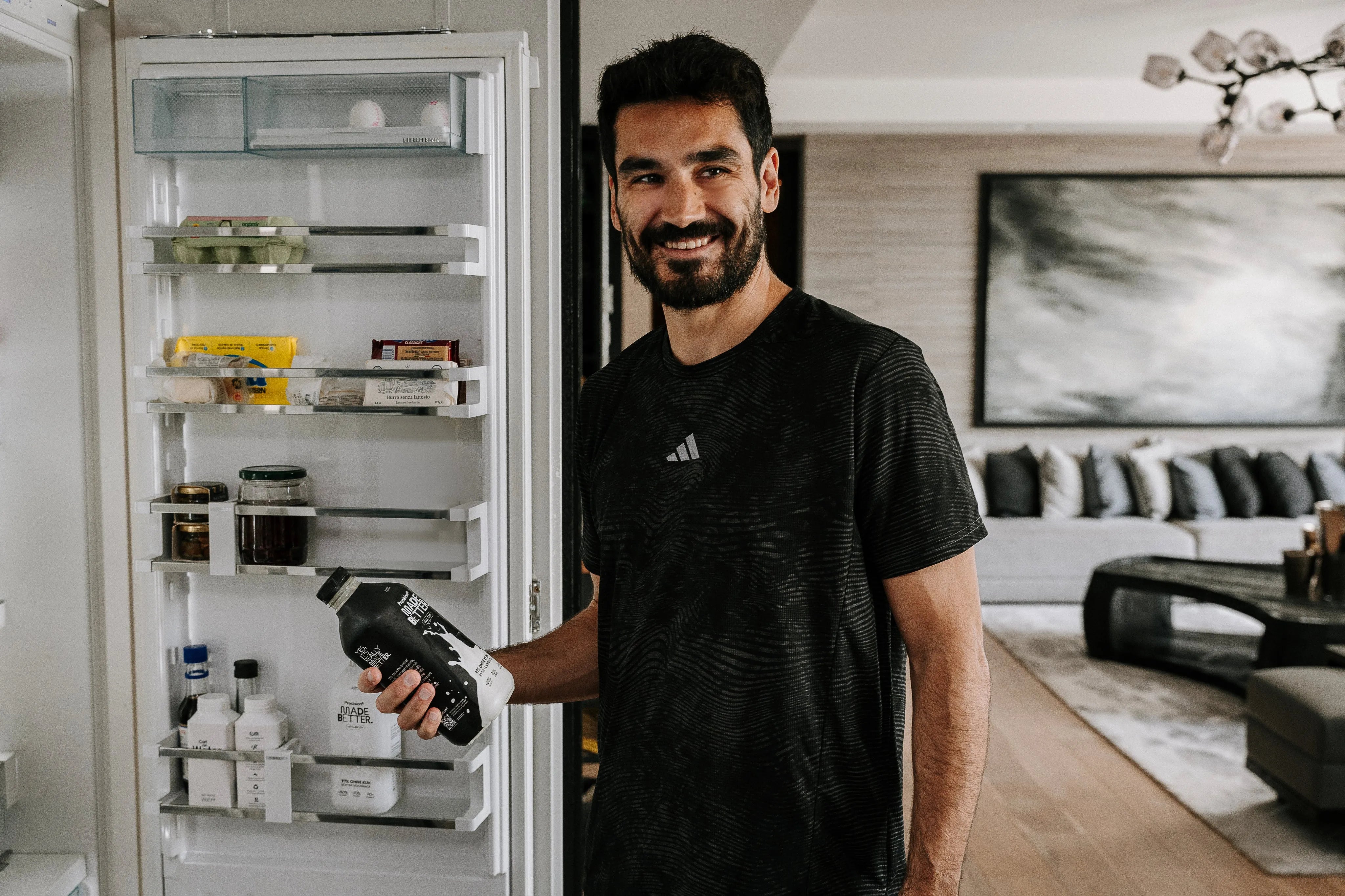 Ein Mann steht vor einem offenen Kühlschrank und hält eine Flasche in der Hand.