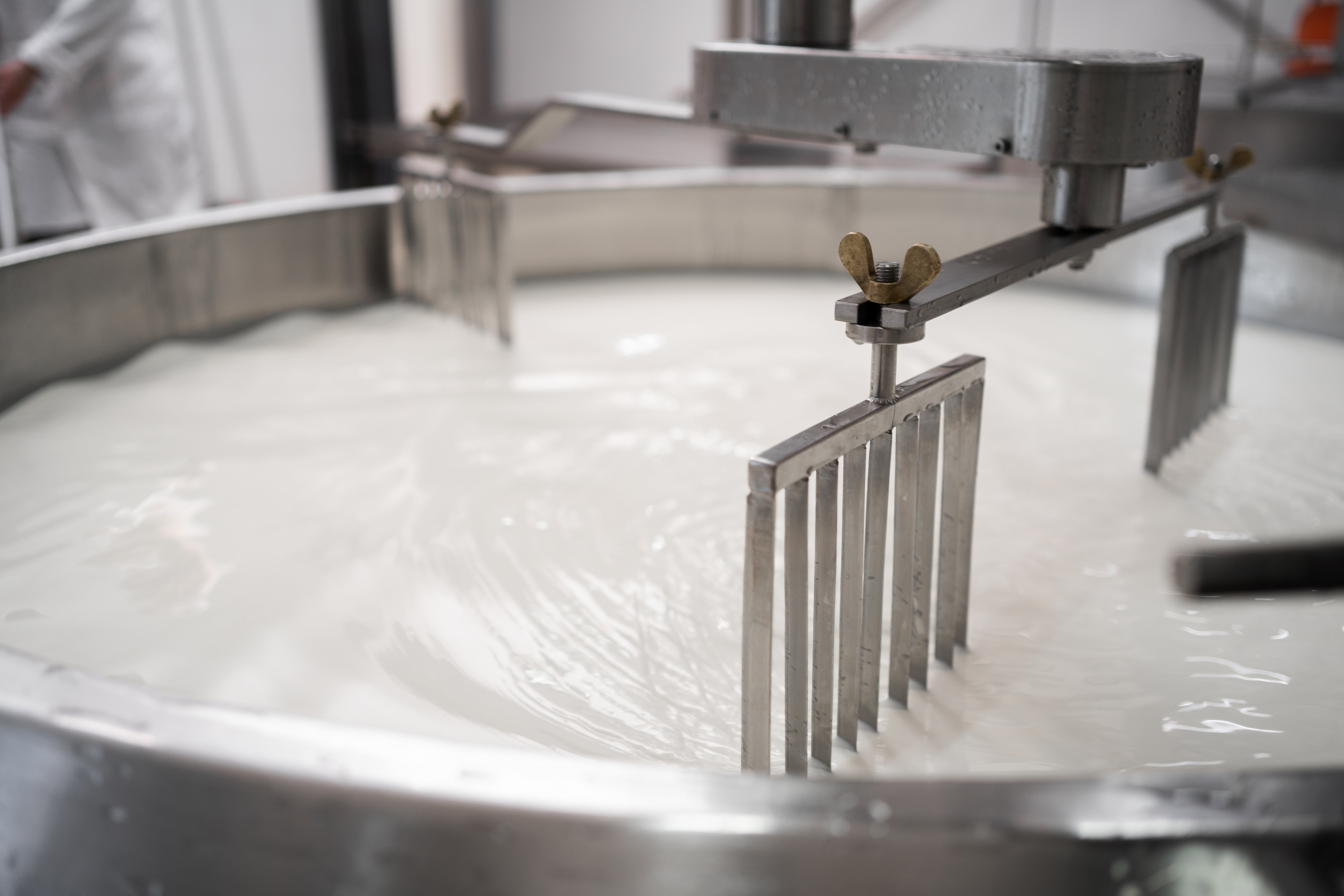 Großer Edelstahltank mit Milch, in dem ein mechanisches Rührgerät die Flüssigkeit umrührt.